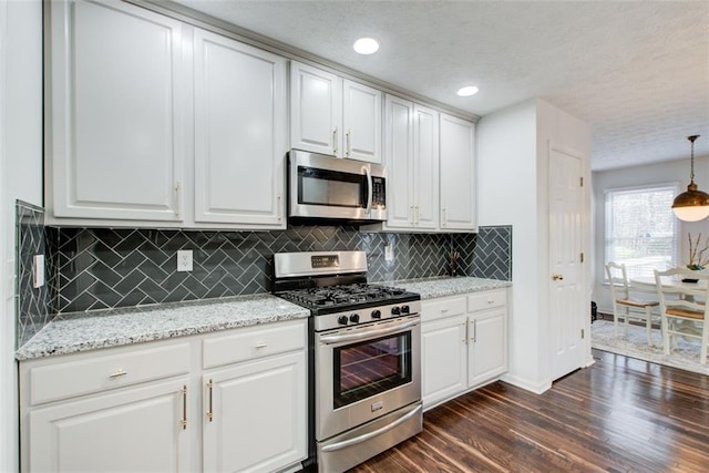 kitchen with white cabinetry, stainless steel appliances, dark hardwood / wood-style floors, decorative light fixtures, and decorative backsplash