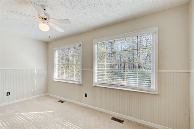 carpeted empty room with ceiling fan, a textured ceiling, and a wealth of natural light