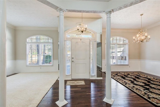 foyer entrance featuring decorative columns, crown molding, and a notable chandelier