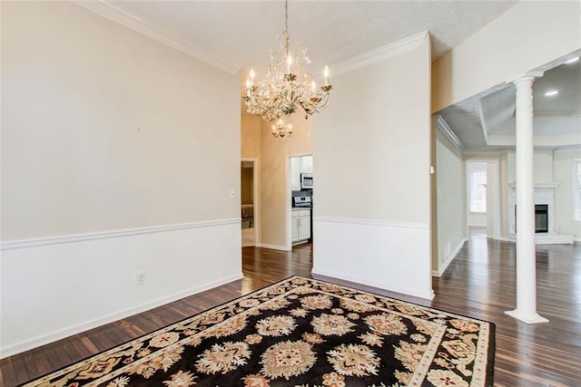 empty room with dark wood-type flooring, decorative columns, an inviting chandelier, and crown molding