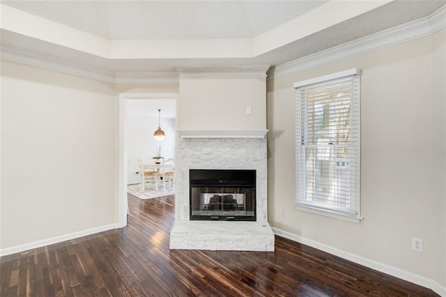 unfurnished living room with dark hardwood / wood-style floors, a stone fireplace, crown molding, and a tray ceiling