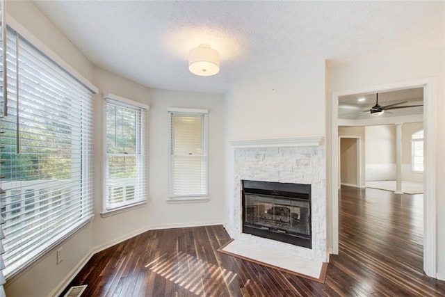 unfurnished living room with ceiling fan, a fireplace, dark wood-type flooring, and a textured ceiling