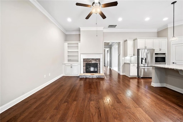 unfurnished living room featuring crown molding, ceiling fan, visible vents, dark wood-type flooring, and a stone fireplace