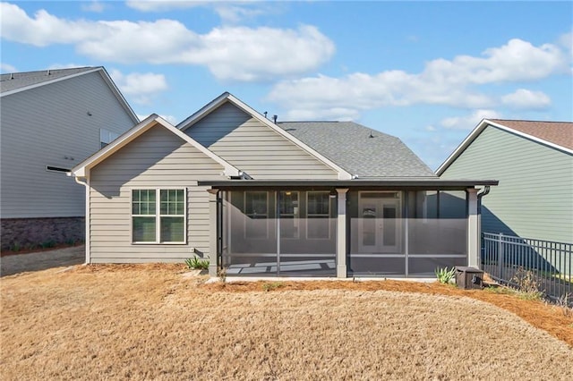 rear view of house with fence, a yard, a shingled roof, and a sunroom