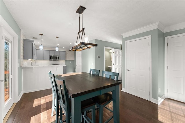 dining room with dark wood-type flooring, crown molding, and sink