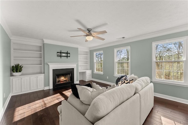 living room with built in features, ceiling fan, crown molding, dark wood-type flooring, and a textured ceiling