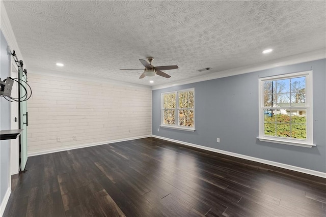 spare room featuring ceiling fan, dark wood-type flooring, a barn door, and a textured ceiling