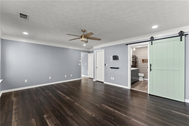 unfurnished living room with a textured ceiling, ornamental molding, dark hardwood / wood-style flooring, ceiling fan, and a barn door