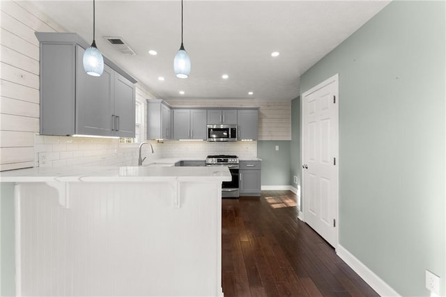 kitchen with a breakfast bar, hanging light fixtures, appliances with stainless steel finishes, gray cabinets, and kitchen peninsula