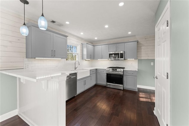 kitchen featuring a kitchen bar, decorative light fixtures, appliances with stainless steel finishes, kitchen peninsula, and gray cabinets