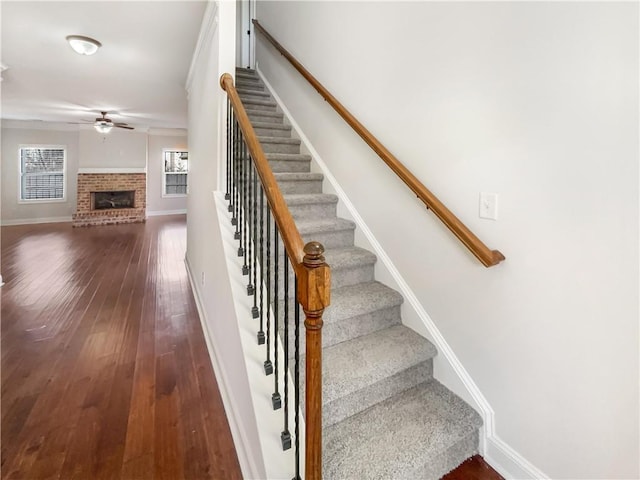 staircase with ceiling fan, a fireplace, and hardwood / wood-style floors