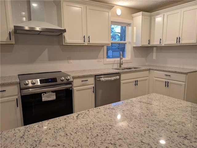 kitchen with white cabinets, wall chimney range hood, sink, light stone counters, and stainless steel appliances