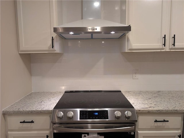 kitchen with wall chimney exhaust hood, light stone counters, white cabinetry, and stainless steel stove