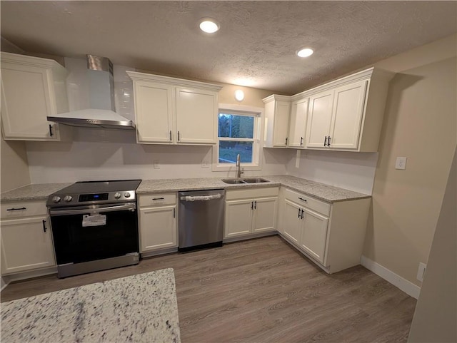 kitchen with wall chimney exhaust hood, stainless steel appliances, sink, hardwood / wood-style flooring, and white cabinets