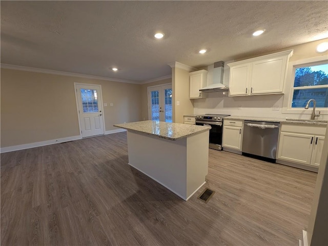 kitchen with light stone counters, wall chimney exhaust hood, stainless steel appliances, sink, and hardwood / wood-style floors