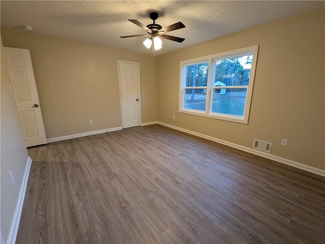 empty room featuring ceiling fan, dark wood-type flooring, and a textured ceiling