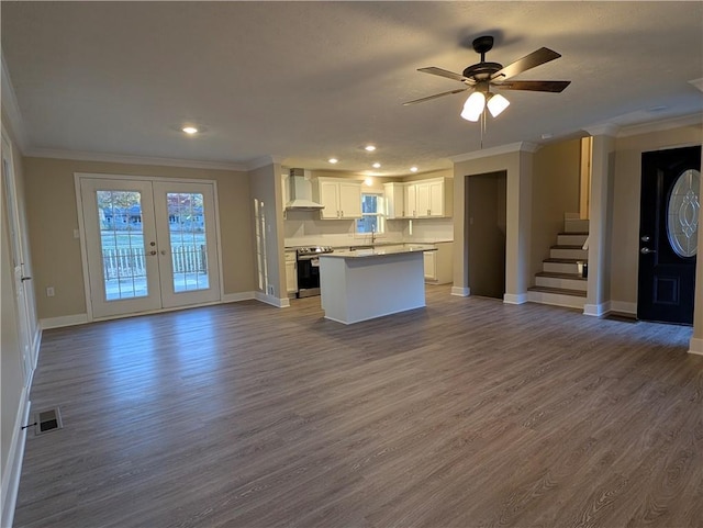 kitchen with white cabinetry, a kitchen island, wall chimney range hood, and light wood-type flooring