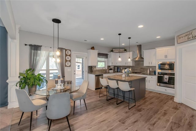 kitchen with white cabinets, wall chimney exhaust hood, stainless steel appliances, and a center island