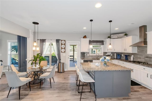 kitchen featuring wall chimney range hood, stainless steel gas cooktop, white cabinets, and a center island