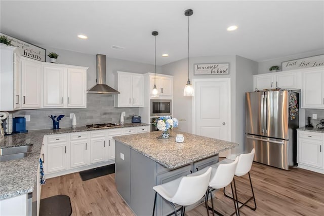 kitchen featuring wall chimney range hood, white cabinetry, a kitchen island, and appliances with stainless steel finishes