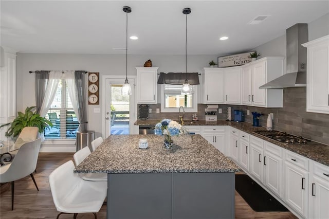 kitchen featuring white cabinets, a center island, wall chimney range hood, stainless steel gas cooktop, and a wealth of natural light