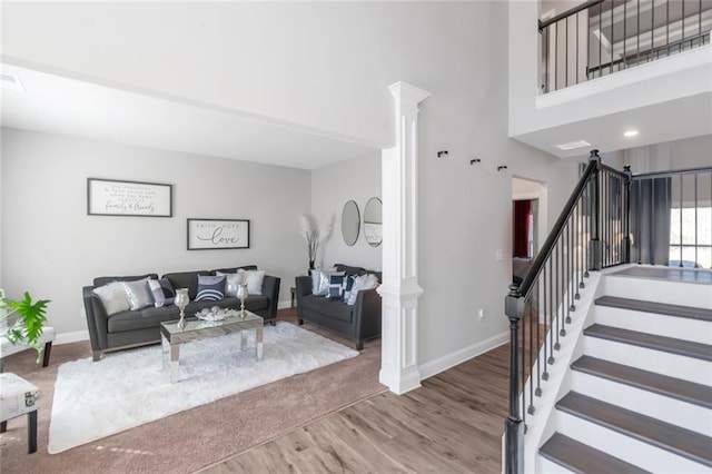 living room featuring ornate columns, stairway, baseboards, and wood finished floors