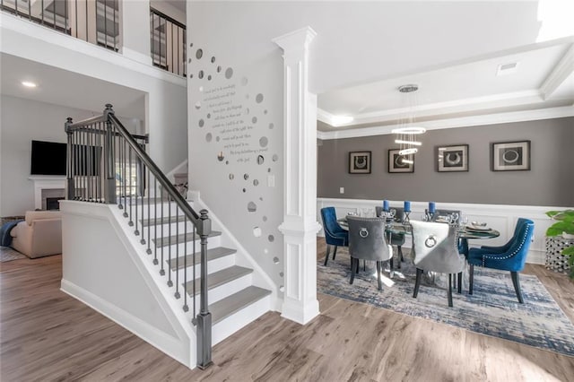 staircase with wood finished floors, a raised ceiling, and ornate columns