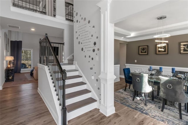 dining area featuring wood finished floors, stairway, a raised ceiling, and ornate columns