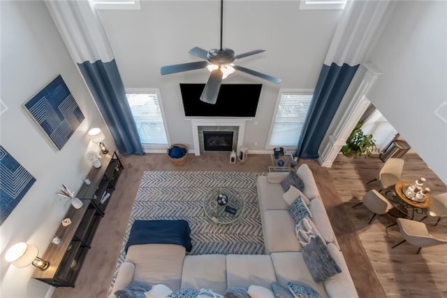 living room with baseboards, a ceiling fan, a towering ceiling, wood finished floors, and a fireplace