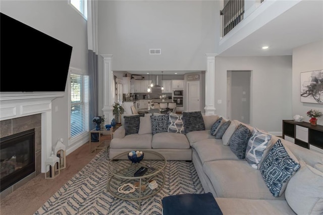 living room with a high ceiling, visible vents, a tiled fireplace, and ornate columns