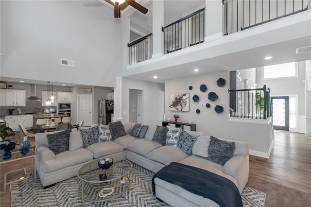 living room featuring visible vents, ceiling fan, wood finished floors, a high ceiling, and ornate columns