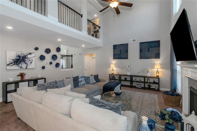 living room featuring a fireplace, visible vents, a towering ceiling, ceiling fan, and wood finished floors