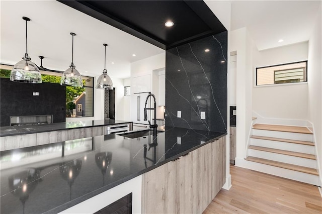 kitchen with dark stone counters, sink, light hardwood / wood-style flooring, decorative light fixtures, and tasteful backsplash