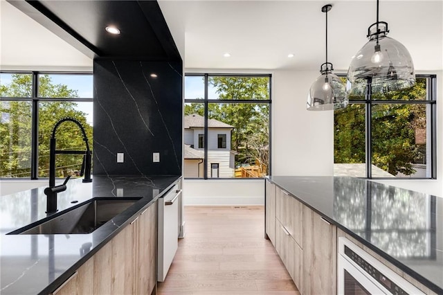 kitchen featuring dark stone countertops, light hardwood / wood-style flooring, pendant lighting, and sink