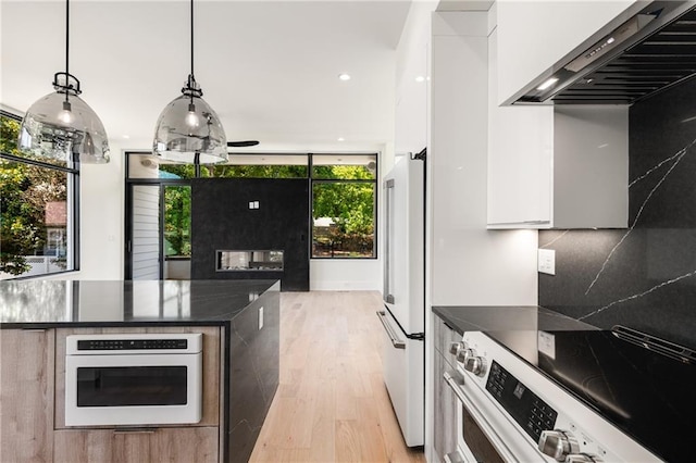 kitchen featuring electric range, custom exhaust hood, white oven, hanging light fixtures, and white cabinets