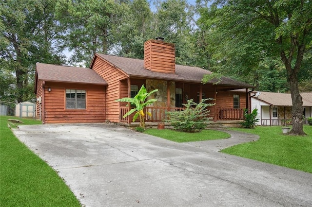 view of front of house with covered porch, a front yard, and a storage shed