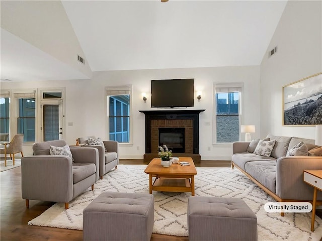 living area featuring high vaulted ceiling, a fireplace, visible vents, and wood finished floors