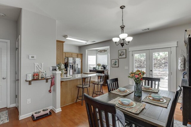 dining area featuring french doors, visible vents, light wood-style flooring, an inviting chandelier, and baseboards