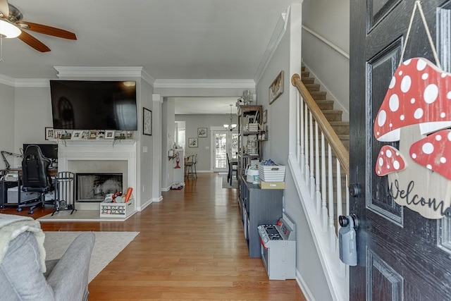 entrance foyer with stairway, a fireplace with raised hearth, wood finished floors, and ornamental molding