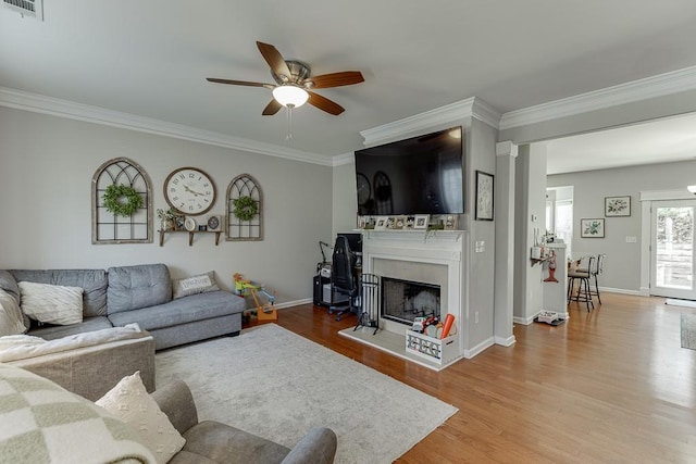 living area featuring a fireplace with raised hearth, ornamental molding, wood finished floors, and baseboards