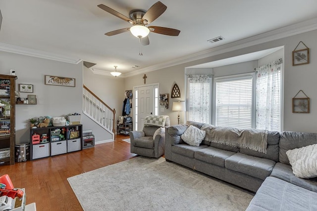 living area with visible vents, ornamental molding, ceiling fan, wood finished floors, and stairs