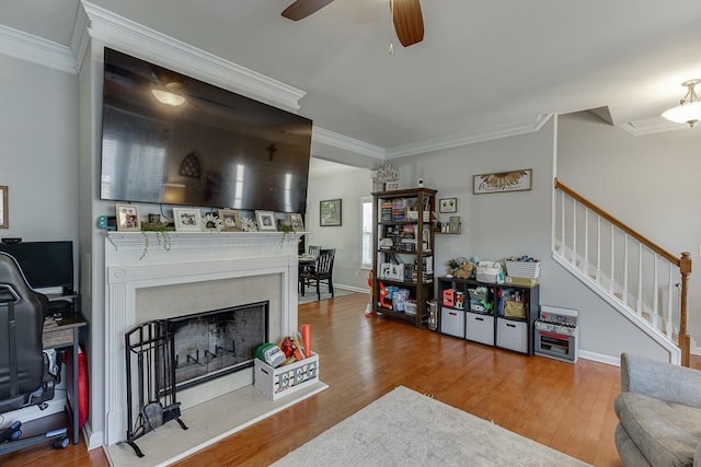 living area with stairs, a fireplace with raised hearth, ornamental molding, and wood finished floors