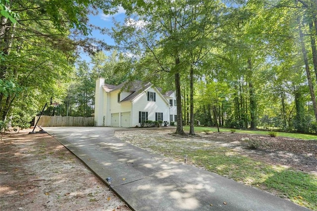 view of property exterior with fence, a garage, driveway, and a chimney