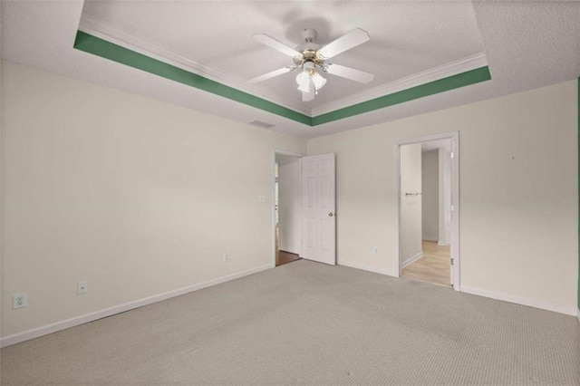 unfurnished bedroom featuring light carpet, ceiling fan, ornamental molding, and a tray ceiling