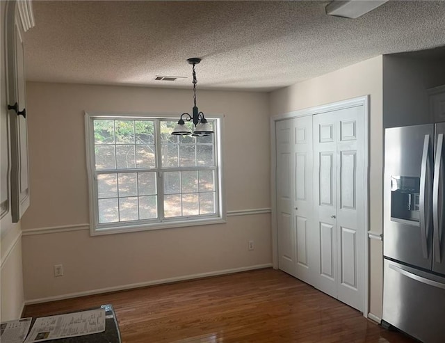 unfurnished dining area featuring a textured ceiling, an inviting chandelier, and dark hardwood / wood-style floors