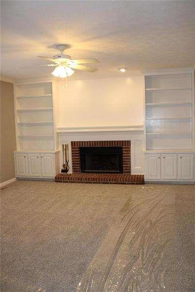 2031 Lakewood Cir, Grayson, GA 30017 - unfurnished living room featuring ceiling fan, a brick fireplace, built in shelves, and light colored carpet
