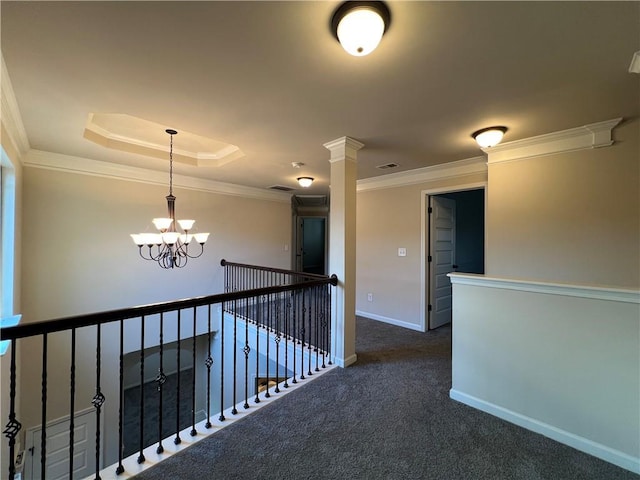 hall with ornate columns, crown molding, a raised ceiling, dark colored carpet, and an inviting chandelier