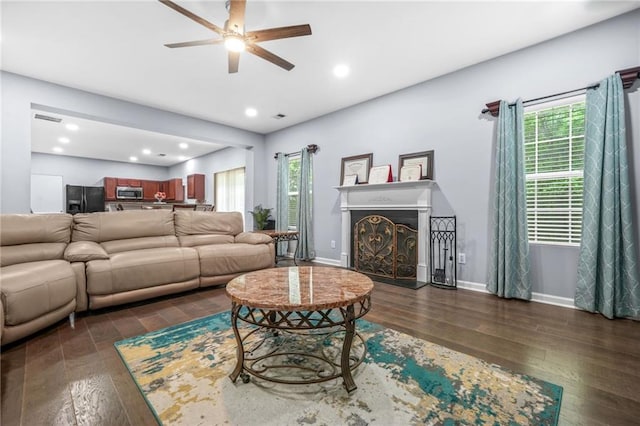 living area with dark wood-style flooring, a ceiling fan, a healthy amount of sunlight, and a fireplace
