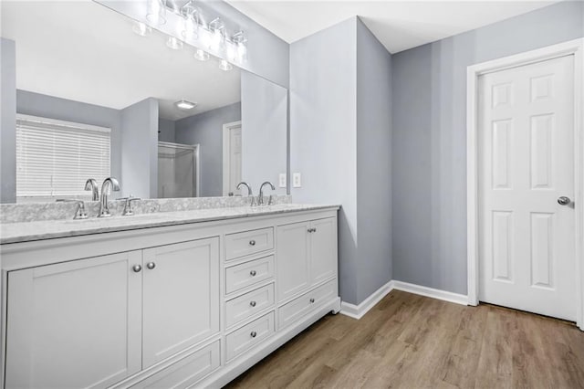 full bath featuring baseboards, a sink, a shower stall, double vanity, and wood finished floors
