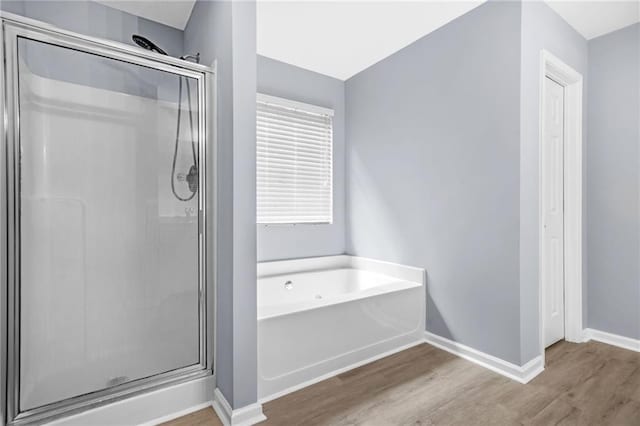 bathroom with a bath, baseboards, wood finished floors, and a shower stall